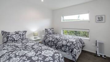 A bedroom with two beds, a nightstand, a lamp, a radiator, and a window with a view.