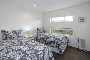 A bedroom with two beds, a nightstand, a lamp, a radiator, and a window with a view. - Number 35, Martinborough (Martinborough)