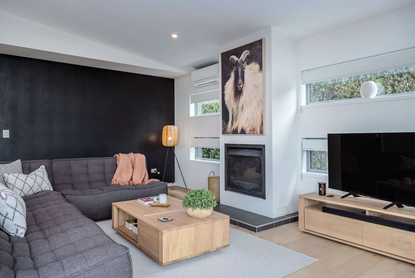 A modern living room with a sectional sofa, a fireplace, a flat-screen TV, and a large window.