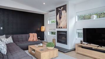 A modern living room with a sectional sofa, a fireplace, a flat-screen TV, and a large window.
