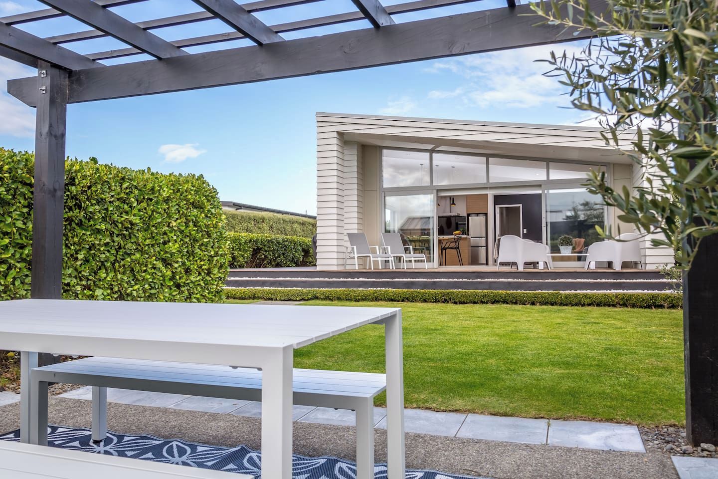 A modern house with a covered patio, a dining area, and a well-maintained lawn.