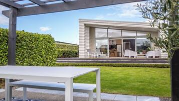 A modern house with a covered patio, a dining area, and a well-maintained lawn.