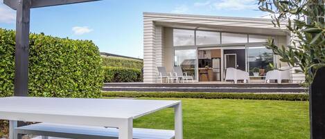 A modern house with a covered patio, a dining area, and a well-maintained lawn.