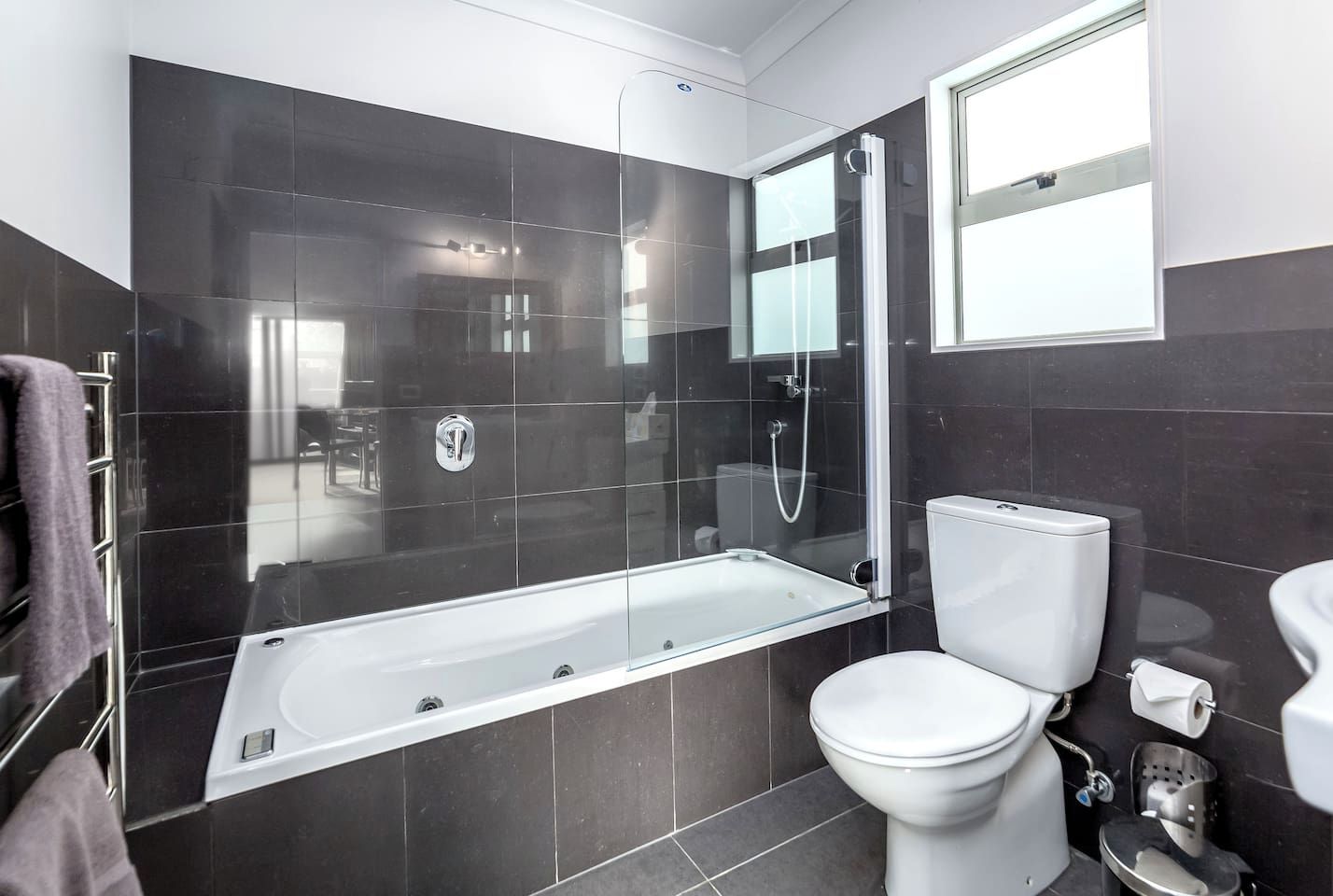 A modern bathroom with a glass-enclosed shower, a white toilet, and a bathtub.