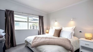A neatly arranged bedroom with a bed, bedside lamps, a nightstand, and a window with curtains. - TWO FOUR COLOGNE#2, Martinborough (Martinborough)
