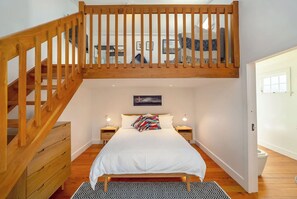 A bedroom with a wooden staircase, a bed with a colorful pillow, bedside tables with lamps, and a black and white patterned rug.