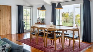 A dining area with a wooden table and chairs, a red rug, and a view of the outdoors through large windows.