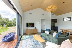A modern living room with a large TV, a sofa set, a wooden coffee table, and a view of the outdoors.