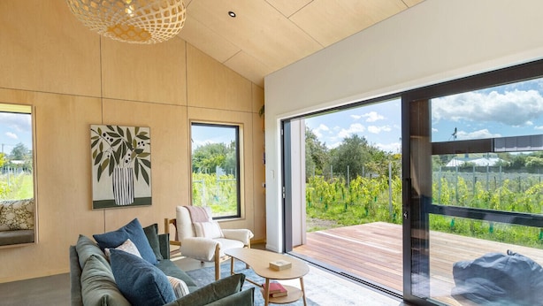 A modern living room with a sofa, a coffee table, and a view of a vineyard through large windows.