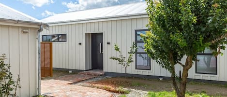 A modern building with a flat roof, a brick pathway leading to the entrance, and a tree in the foreground.