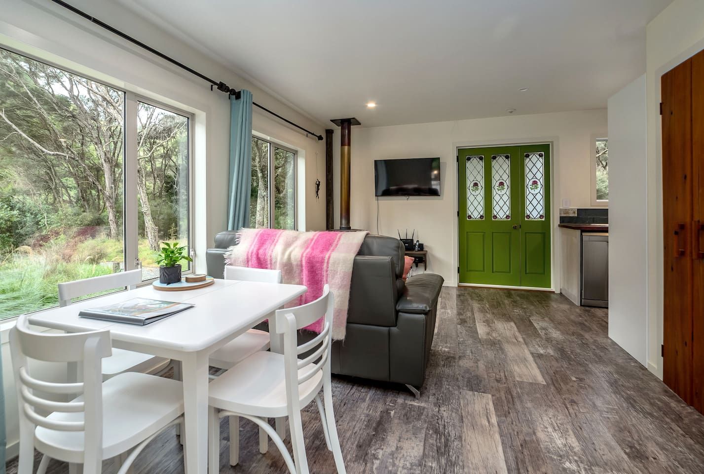 Uma sala de estar moderna com área de jantar, uma porta verde e cozinha ao fundo.