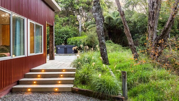 A modern house with a wooden deck leading to a glass door, surrounded by lush greenery and trees. - The Glade, Martinborough (Ruakōkoputuna)