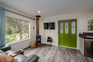 A living room with a fireplace, a television mounted on the wall, and a green door. - The  Glade, Martinborough (Ruakōkoputuna)