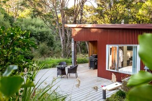 Eine moderne Außenterrasse mit Grill, Sitzgelegenheit und einem wintergartenähnlichen Raum.