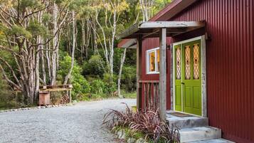 A rustic building with a green door, a wooden porch, and a gravel driveway leading to a wooden bench.