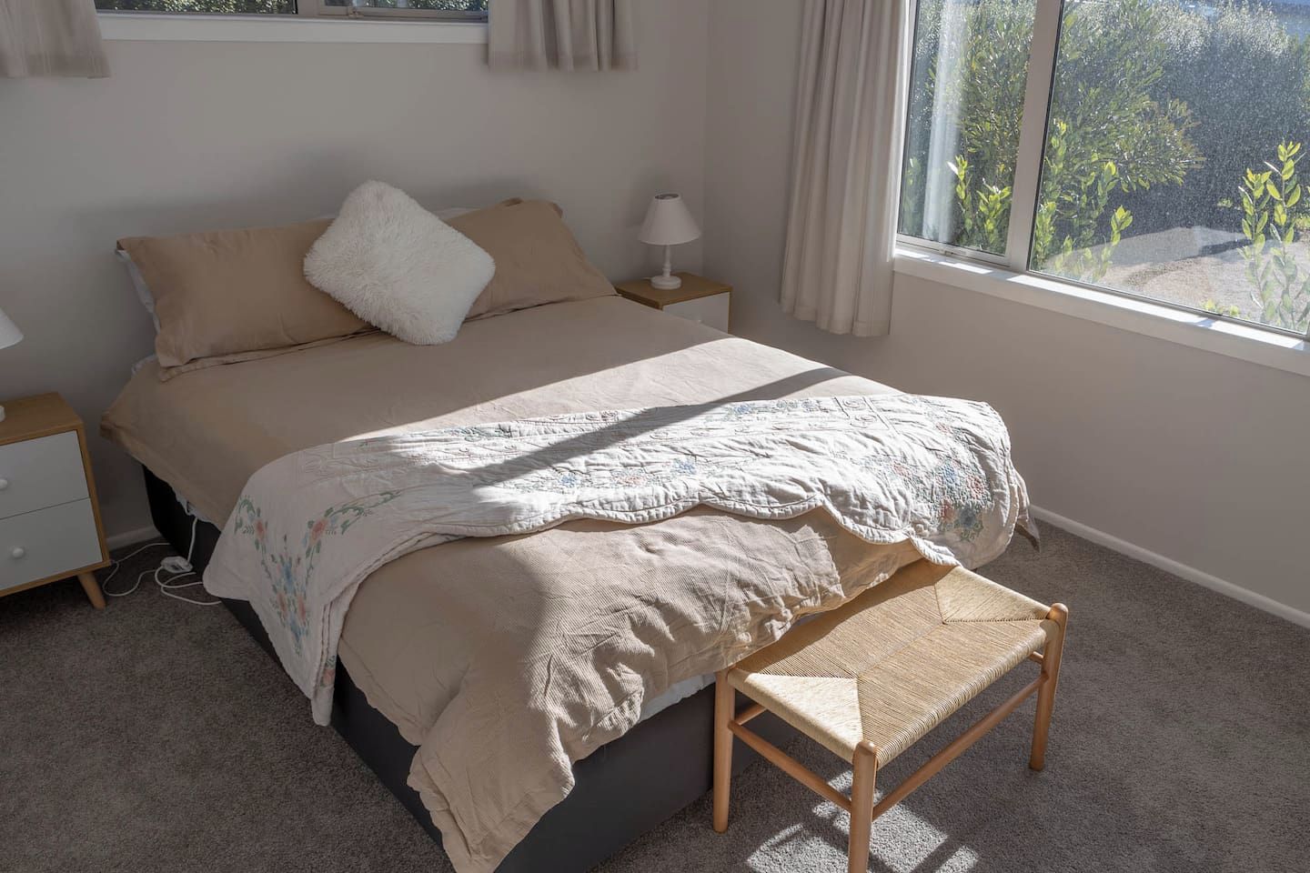 Un dormitorio con cama, mesitas de noche, un banco y una ventana con vistas.