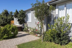 Il s'agit d'une propriété résidentielle dotée d'une allée en gravier, d'une terrasse en bois et d'une variété d'arbustes et de petits arbres.