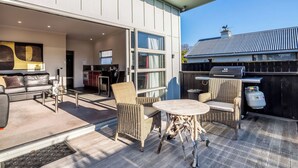 Een terras buiten met een eettafel, stoelen, een bank en een barbecue.