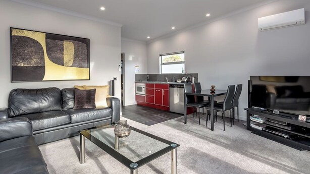 Een moderne woonkamer met een leren bank in zwart, een glazen salontafel en een flatscreen televisie.