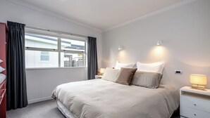 Een slaapkamer met een groot bed, nachtlampjes, een raam met gordijnen en uitzicht op buiten.