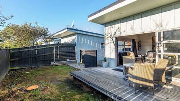 A modern outdoor patio with a wooden deck, wicker furniture, and a glass door leading to an interior space.