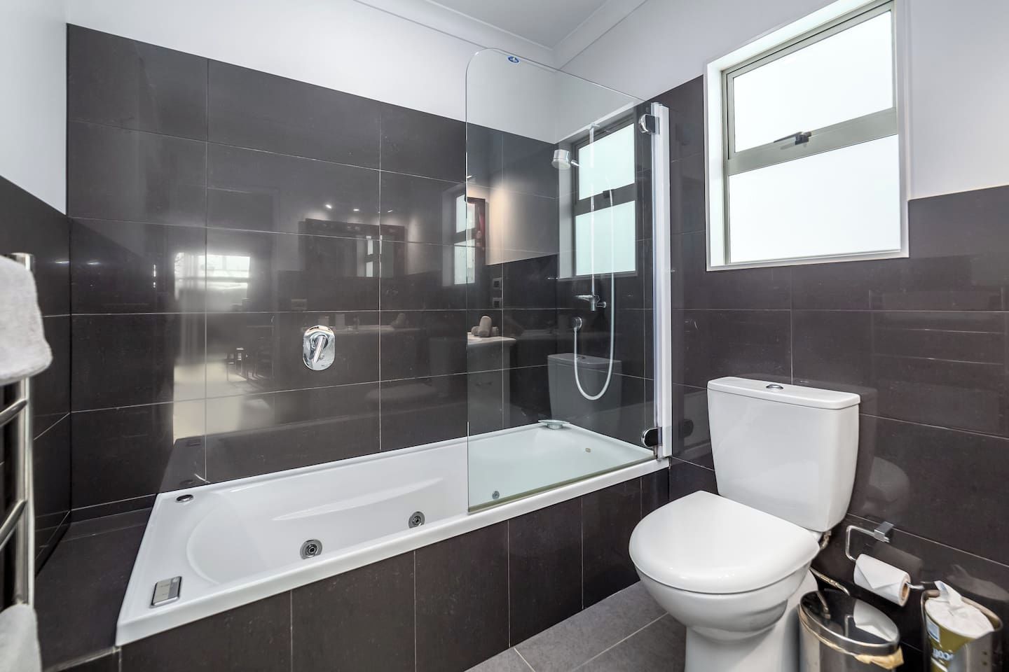 Ein modernes Badezimmer mit einer gläsernen Dusche, einer weißen Toilette und einem großen Fenster.