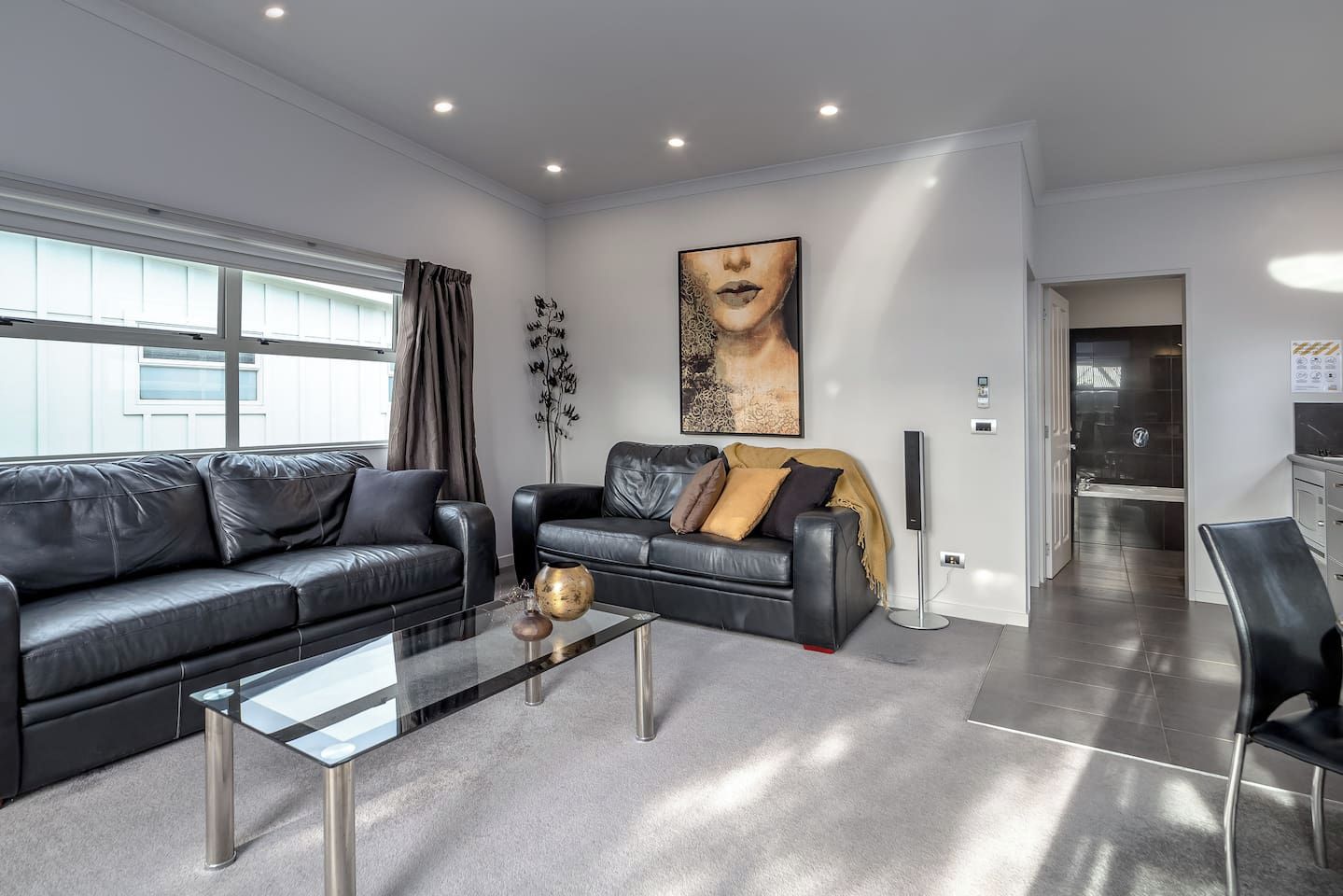 A modern living room with two black leather sofas, a glass coffee table, and a large abstract painting on the wall.