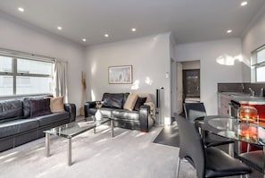 A modern living room with a sofa, coffee table, and chairs. There is a kitchen area with a sink and a dining table. - Two Four Cologne #3, Martinborough (Martinborough)