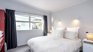 Een hotelkamer met een groot bed, een nachtkastje met een lamp, een rode garderobe en een raam met gordijnen.