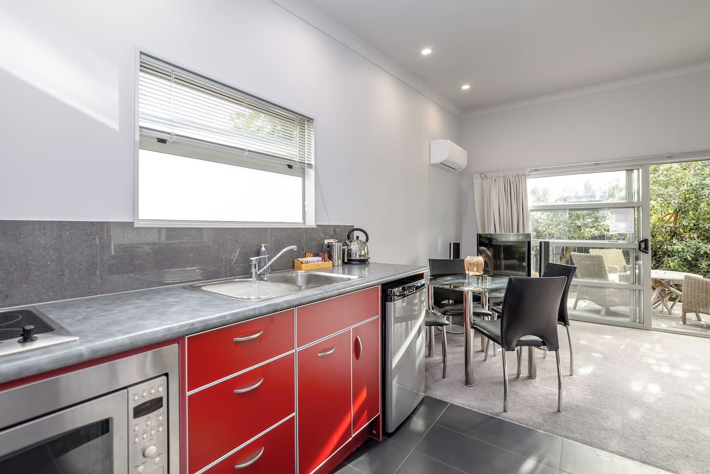 A modern kitchen with a built-in oven, a sink, and a dining area with a glass table and chairs.