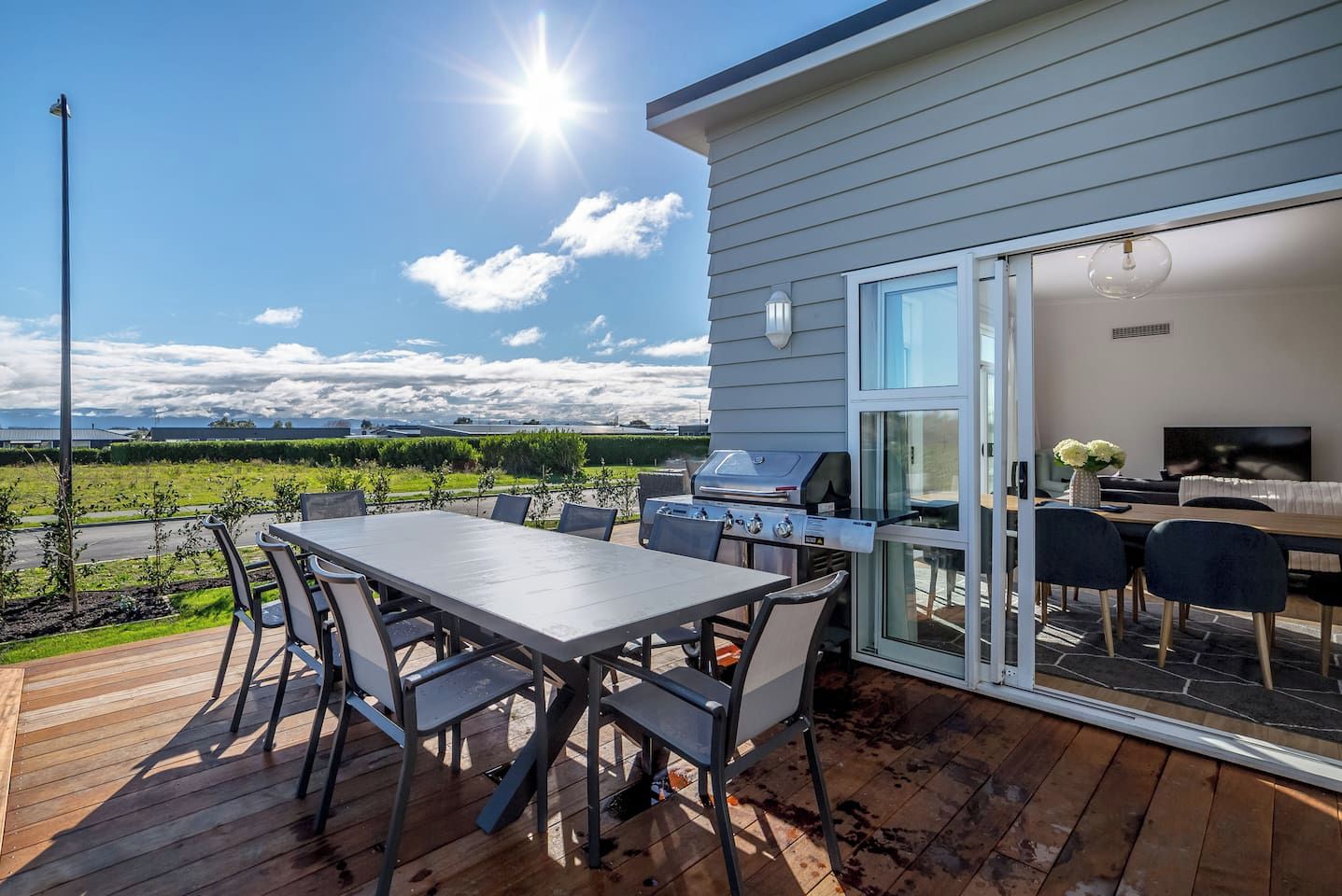 A deck with a table and chairs, a grill, and a glass door leading to a living area with a TV.