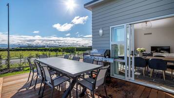 A deck with a table and chairs, a grill, and a glass door leading to a living area with a TV.