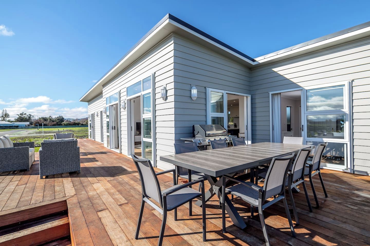 A modern house with a deck, outdoor seating, and a barbecue area.