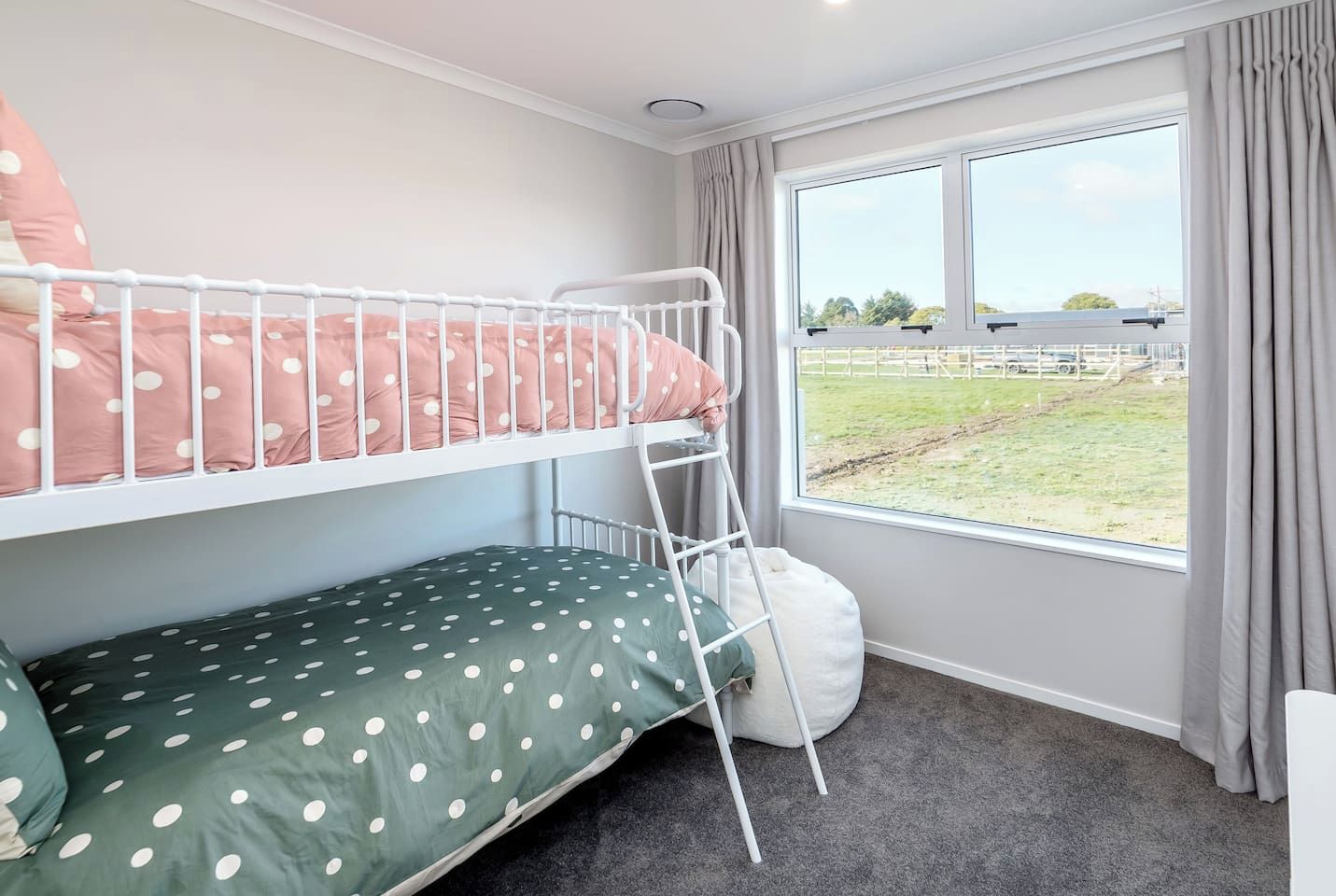 A bunk bed room with a view of a grassy field and a fence.