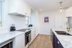 Eine moderne Küche mit weißen Schränken, einer schwarzen Induktionskochplatte, einem Backofen und einer Spüle mit Goldarmatur.