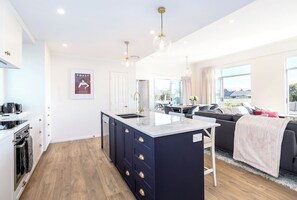 A modern kitchen with a central island, a dining area with a sofa, and a view of the outdoors. - Three on Wilson, Martinborough (Martinborough)