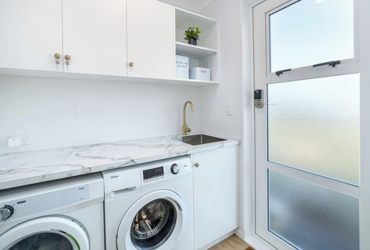 Une cuisine compacte équipée d’un lave-linge, d’un évier et d’un plan de travail en marbre.