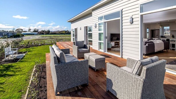 A modern house with a wooden deck, outdoor seating, and a large sliding glass door leading to an interior space. - Three on Wilson | Modern 4BR, Seasonal Communal Pool Access & Walk to Town (Martinborough)