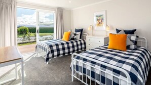 A bedroom with two beds, a desk, and a window with a view of the outdoors. - Three on Wilson | Modern 4BR, Seasonal Communal Pool Access & Walk to Town (Martinborough)