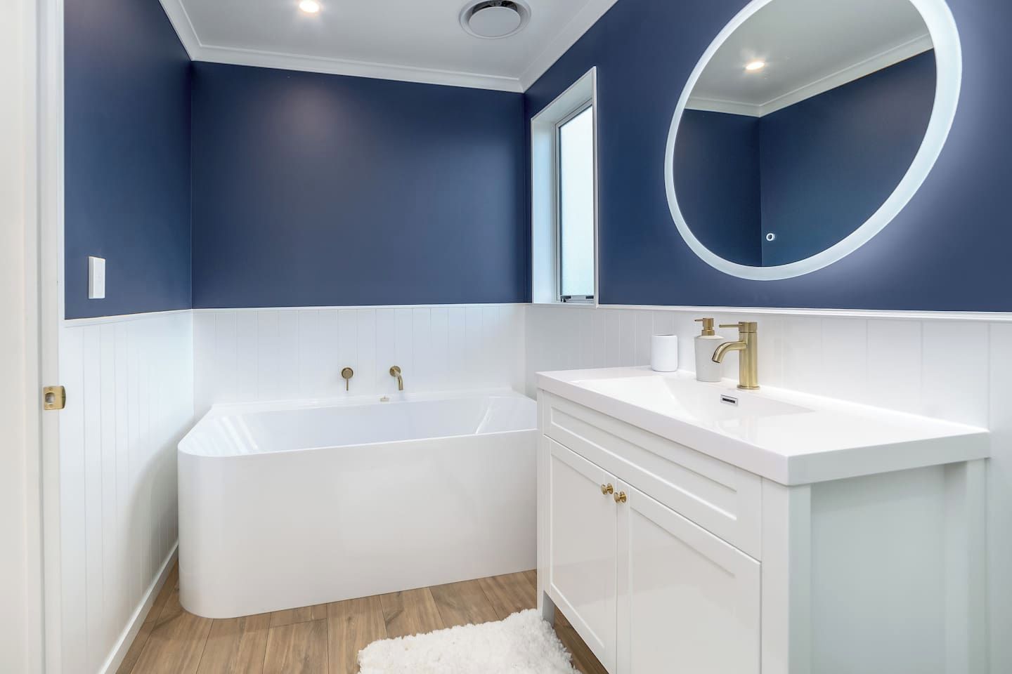 A modern bathroom with a freestanding bathtub, a white vanity with gold handles, and a round mirror with a white frame.