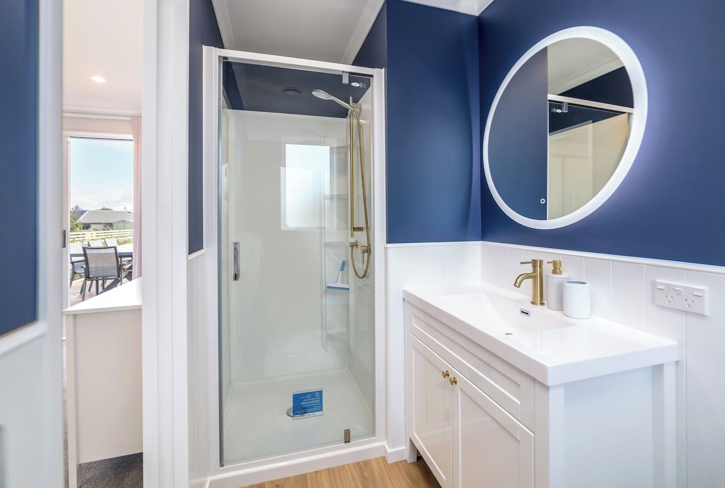 A modern bathroom with a glass-enclosed shower, a white vanity with gold fixtures, and a large mirror.