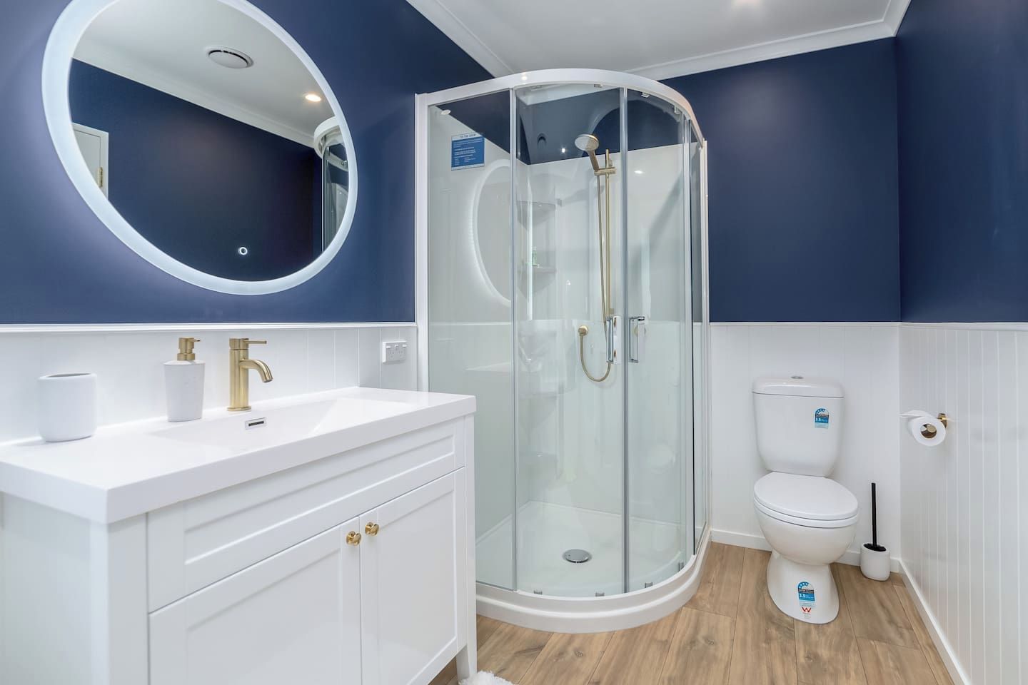 A bathroom with a glass-enclosed shower, a white sink with gold fixtures, and a toilet with a white lid.
