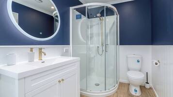 A bathroom with a glass-enclosed shower, a white sink with gold fixtures, and a toilet with a white lid.