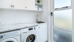 A compact kitchen with a built-in washer and dryer, white cabinetry, a marble countertop, and a frosted glass door. - Three on Wilson | Modern 4BR, Seasonal Communal Pool Access & Walk to Town (Martinborough)