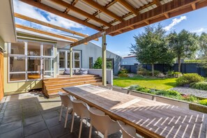 An outdoor patio with a wooden table and chairs, a covered seating area, and a view of a garden and house. - Family Retreat, Martinborough (Martinborough)