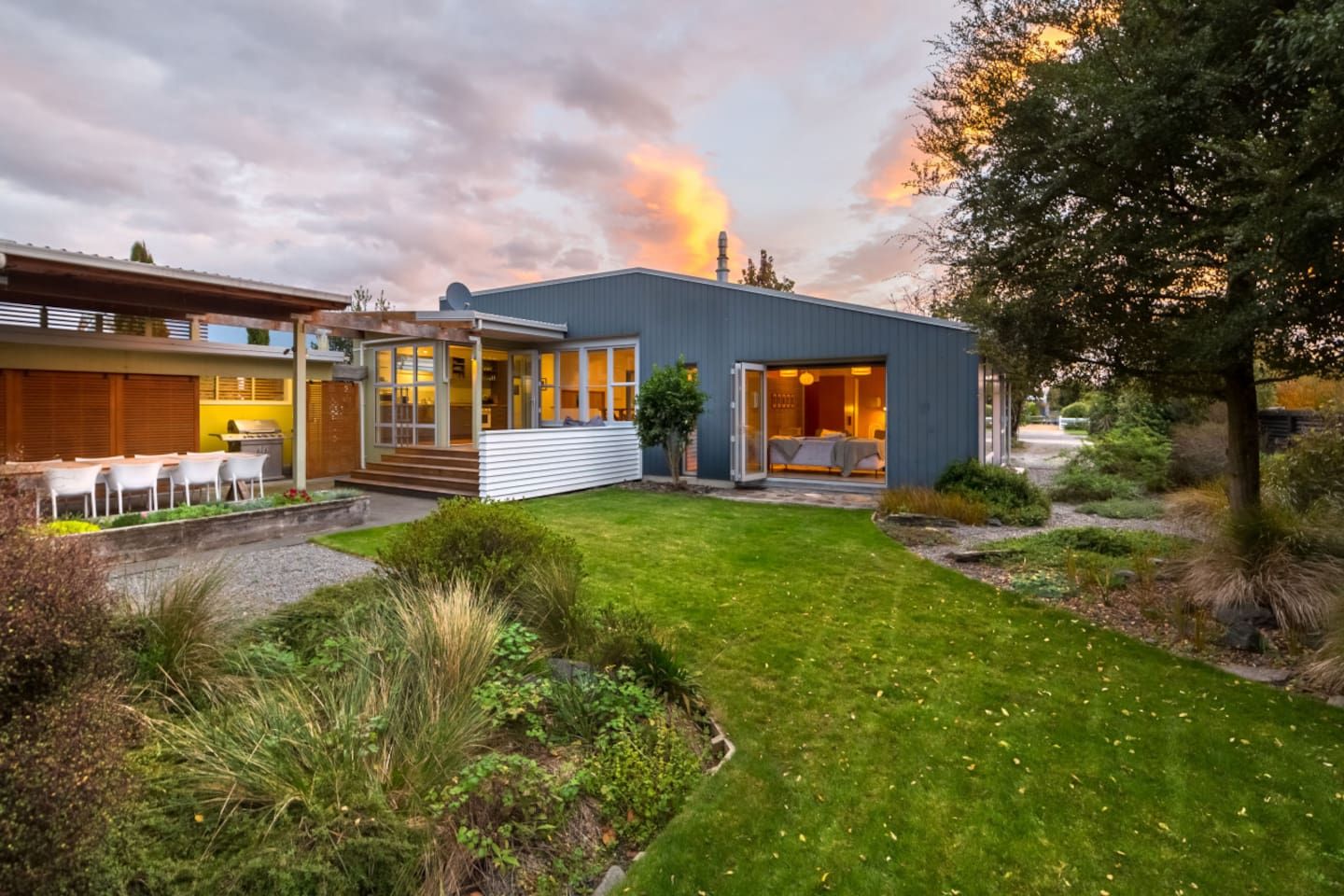A modern house with a well-maintained lawn, a patio with outdoor furniture, and a large open window.