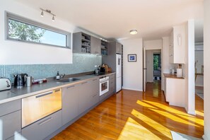 A modern kitchen with a large window, grey cabinetry, a built-in oven, and a wooden floor.