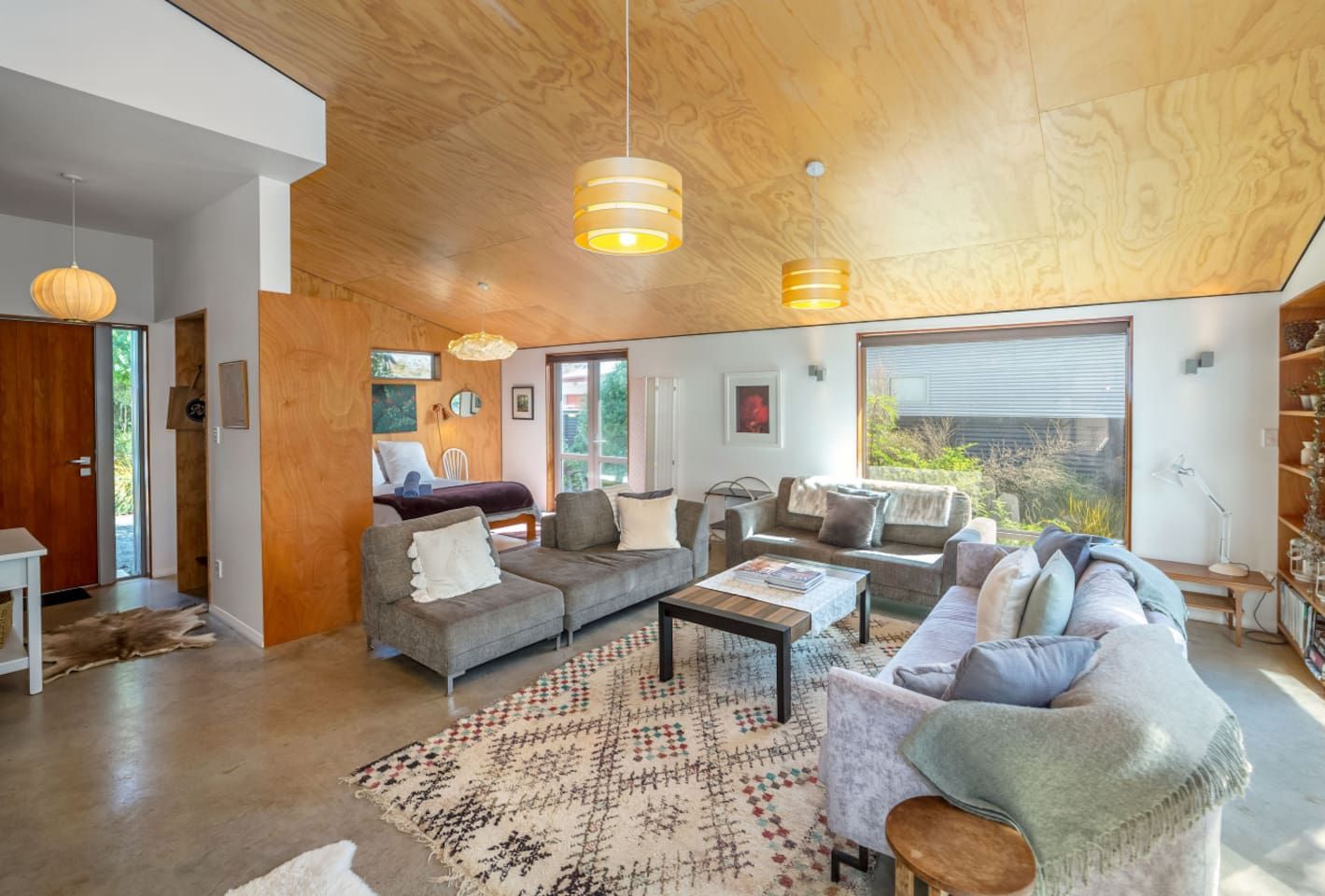 A modern living room with a large sofa, a coffee table, and a rug. There are two pendant lights hanging from the ceiling.