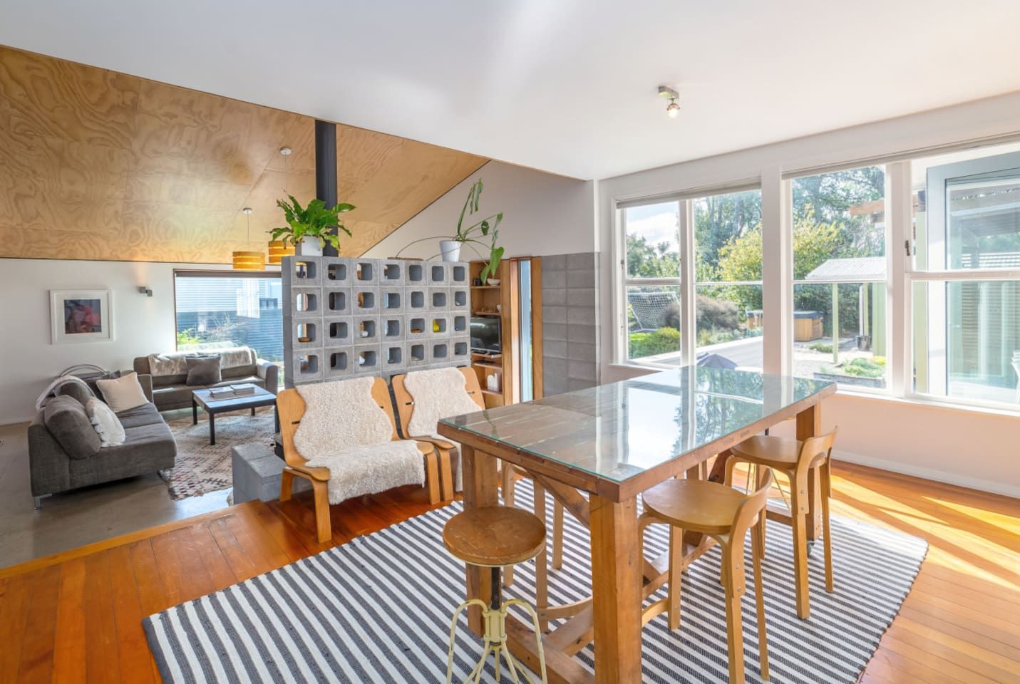 Un espace de vie moderne avec une table à manger en verre, des chaises en bois, un canapé gris et un tapis à rayures.