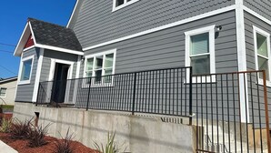 Una casa a due piani con facciata grigia e tetto rosso, con un vialetto in cemento e una recinzione in metallo.